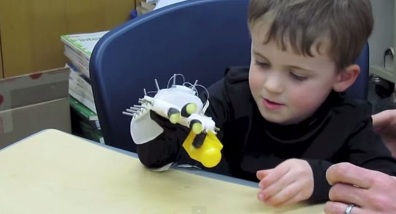 A child trying a robotic hand while seated at a table.